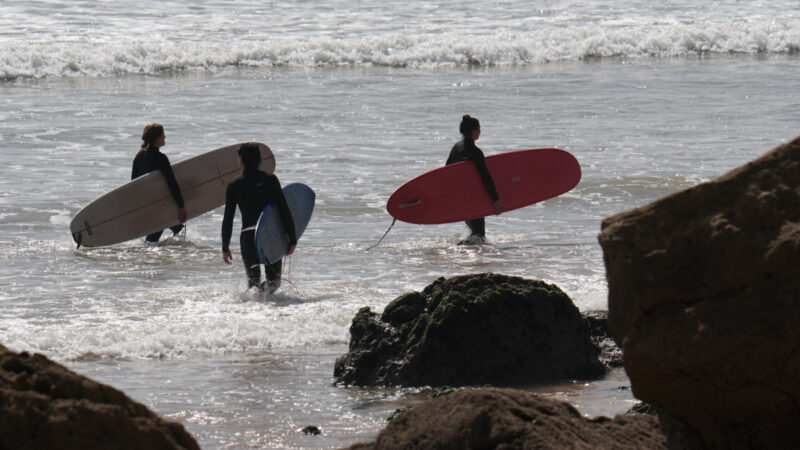 3 people in a surfing lesson walking across the bay in high tide